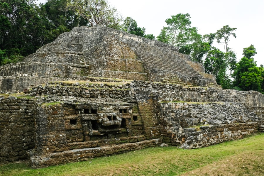 The Jaguar Temple, an ancient Mayan pyramid structure, featuring carved jaguar motifs and stepped terraces, surrounded by dense jungle at the Lamanai archaeological site in Belize.