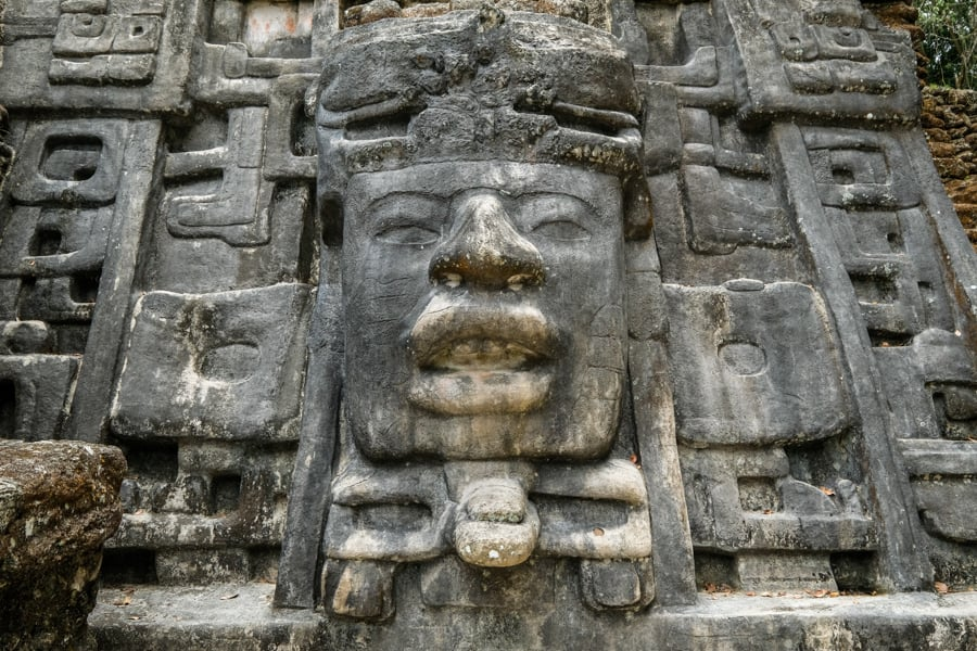 Close-up of an intricately carved stone face at Lamanai, showcasing detailed Mayan artistry with bold facial features, part of the ancient temple ruins in Belize.