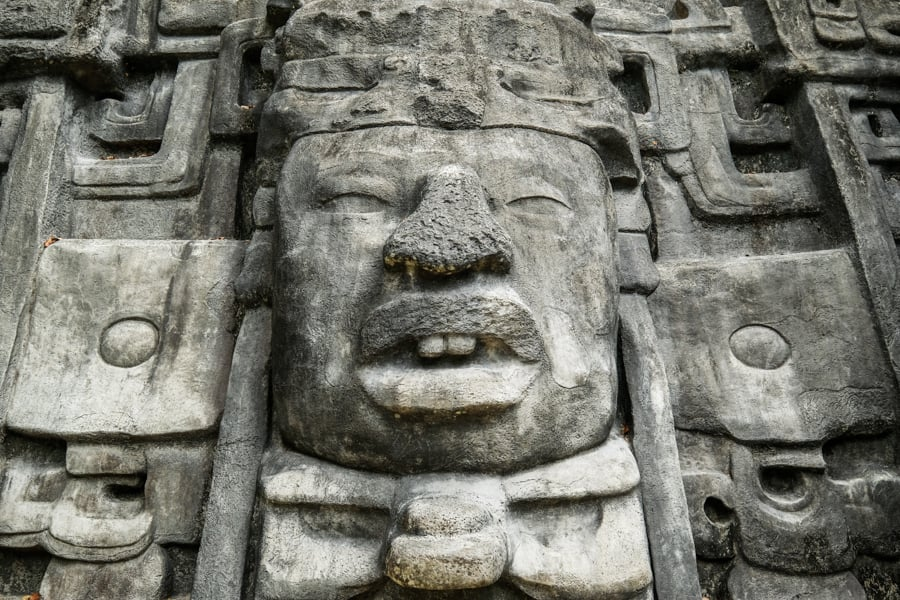 Stone-carved face on the Mask Temple at the Lamanai Mayan ruins, featuring intricate ancient Mayan artistry with bold facial features, part of the ceremonial architecture in Belize.